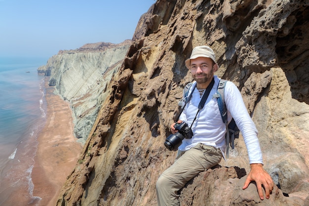 Erfreulicher Reisender mit Kamera sitzt am Rand der Klippe, Hormuz Island, Hormozgan, Iran.