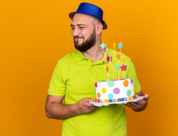 Erfreut aussehender junger Mann mit Partyhut, der Kuchen hält