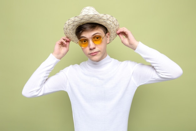 Erfreut junger gutaussehender Kerl mit Hut mit Brille isoliert auf olivgrüner Wand