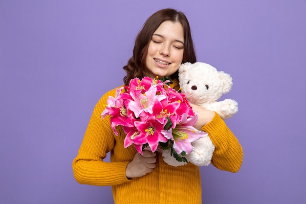 Erfreut mit geschlossenen Augen schönes junges Mädchen mit Blumenstrauß mit Teddybär