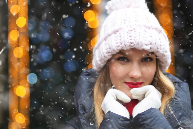 Erfreute blonde Frau trägt Strickmütze zu Fuß auf der Wintermesse bei Schneefall. Leerer Platz für Text