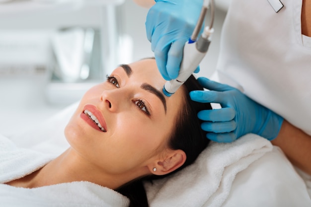 Erfreute nette Frau, die lächelt, während sie hydrafacial Prozedur genießt