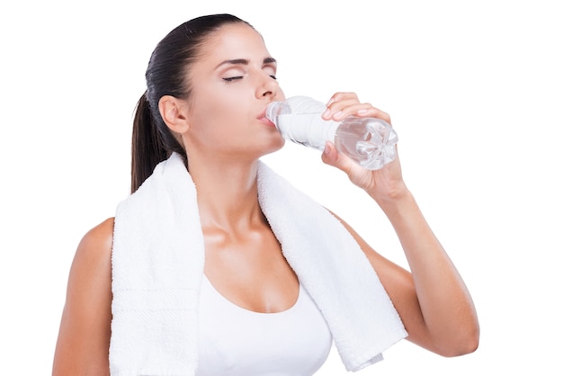 Erfrischend nach dem Training. Müde junge Frau, die eine Flasche mit Wasser hält und ihre Stirn mit der Hand berührt, während sie isoliert auf weiß steht