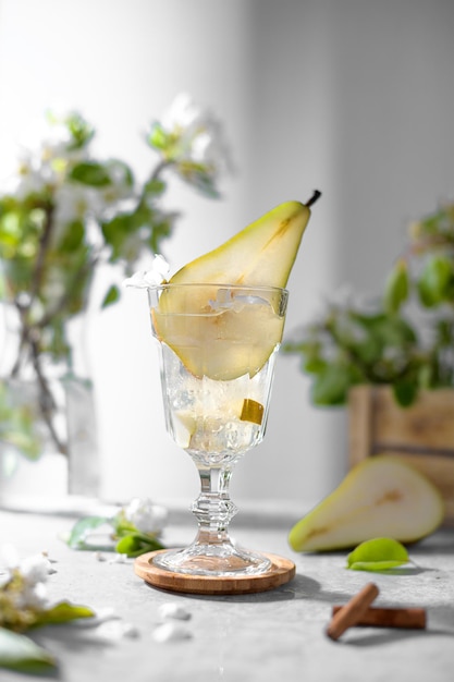 Erfrischende Birnencocktaillimonade in einem Glas mit Birnenpüree und frischem Obst und Blumen auf hellgrauem Tischhintergrund