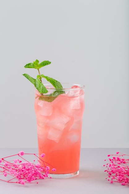 Erfrischende Cocktailrose mit Traubensirup und Minzrosenblüten neben dem Glas auf grauer High...