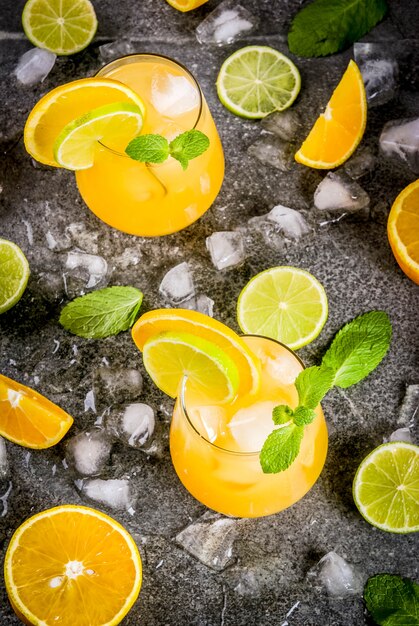 Erfrischende Sommergetränke mit Vitaminen. Zitruspunsch mit Orangen und Limette, mit Minzezweigen, mit Eis gekühlt. Auf schwarzem Steintisch, mit Zutaten,