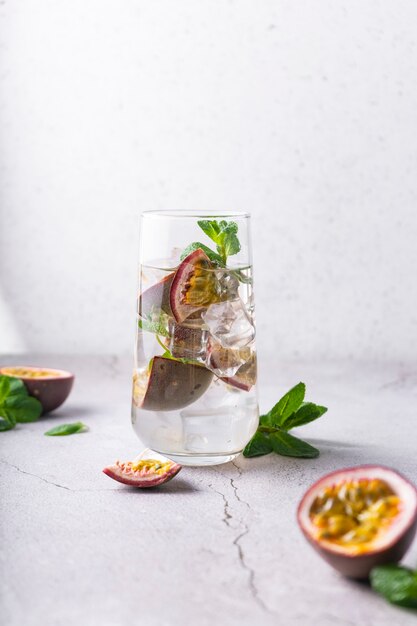 Erfrischendes Getränk mit Passionsfruchtcocktail mit tropischen Früchten auf einer hellen Oberfläche mit vertikaler Position der grünen Minzblätter