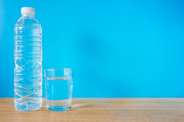 Erfrischendes natürliches Mineralwasser in Plastikflasche mit transparentem Glas auf Holzschreibtisch