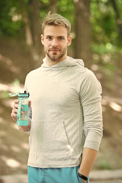 Erfrischendes Vitamingetränk nach dem Training im Freien Man sportliches Aussehen hält Wasserflasche Guy Athlet hält Flasche Pflege Hydratation Körper nach dem Training Athlet trinkt Wasser nach dem Training im Park