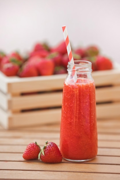 Erfrischungsgetränk Erdbeer-Smoothie in einer Mini-Glasflasche mit einem Strohhalm auf einem Holztisch