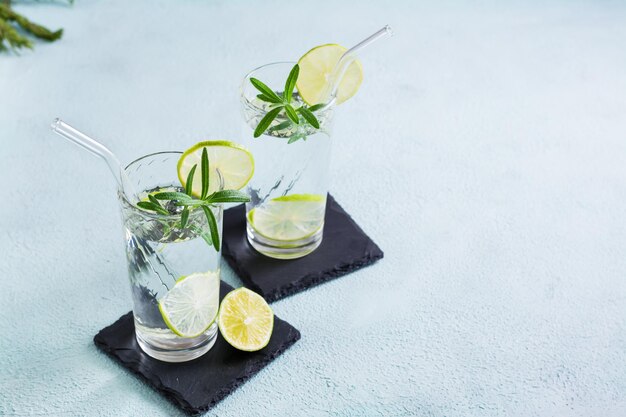 Erfrischungsgetränk Mineralwasser mit Limette und Rosmarin in Gläsern mit Öko-Stroh auf dem Tisch