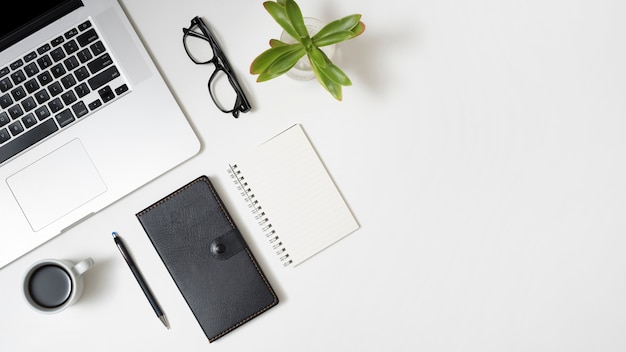 Erhöhte Ansicht des Laptops; Kaffeetasse; Tagebuch; Brillen und Topfpflanze über Business Desk