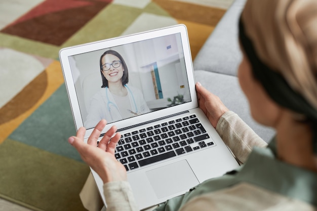 Erhöhte Ansicht einer Frau, die mit einer jungen Ärztin auf dem Laptop-Bildschirm per Video-Chat spricht, Kopienraum