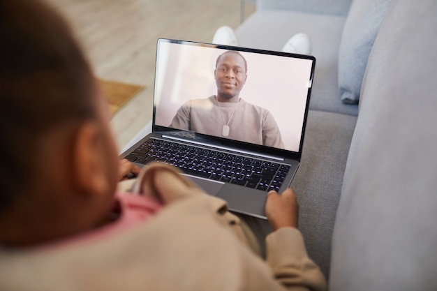 Erhöhte Ansicht eines afroamerikanischen Mädchens, das per Video-Chat mit Papa spricht, während es sich sozial distanziert, Platz kopieren