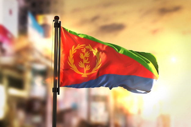 Eritrea-Flagge gegen Stadt verschwommen Hintergrund bei Sonnenaufgang Hintergrundbeleuchtung