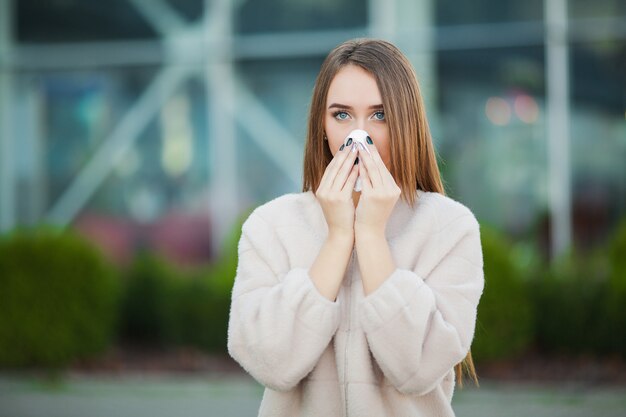 Erkältung und Grippe. Junges attraktives Mädchen, erkältet auf der Straße, wischt sich mit einer Serviette die Nase