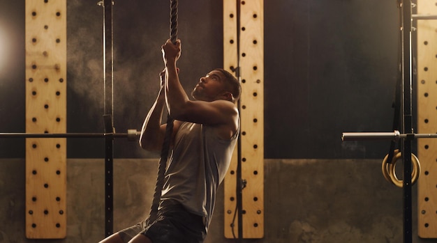 Erklimmen Sie Ihren Weg nach oben Aufnahme eines muskulösen jungen Mannes, der in einem Fitnessstudio an einem Seil klettert