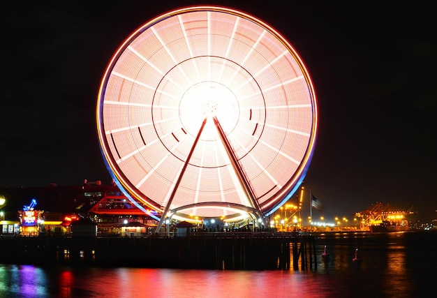 Erleuchtetes Riesenrad am Fluss gegen den Nachthimmel