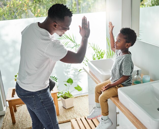 Ermutigen Sie Ihr Kind, gute Hygienepraktiken zu befolgen Hochwinkelaufnahme eines Vaters, der seinem Sohn in einem Badezimmer zu Hause ein High Five gibt