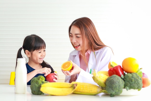 Ernährung für Schulkinder Eine schöne Ernährungsberaterin oder Ärztin erklärt einem kleinen Mädchen die Vorteile von Obst und Gemüse. Die Auswahl der richtigen Lebensmittel entsprechend dem Alter des Kindes