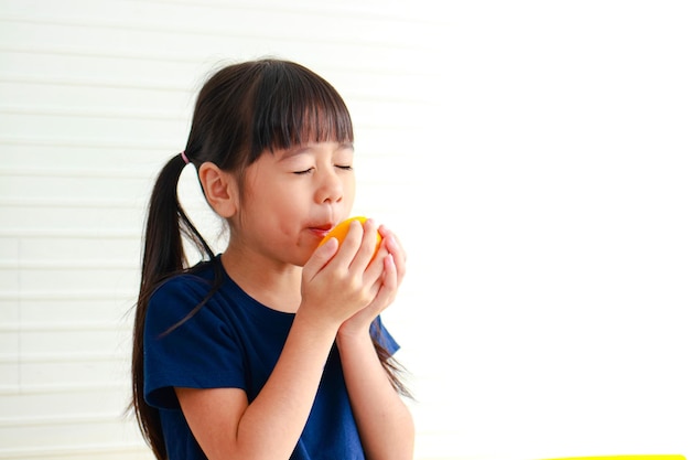 Ernährung für Schulkinder Süße kleine Asiatin isst gerne Orangen Auswahl der richtigen Nahrung je nach Alter des Kindes für eine gute Gesundheit