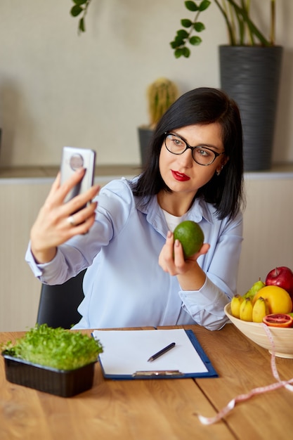 Ernährungsberaterin, Diätassistentin, die auf einem Smartphone ihren Vlog über gesunde Ernährung, Gesundheits- und Ernährungskonzept aufzeichnet. Ernährungsberaterin mit Früchten, die zu Hause an ihrem DES arbeiten.