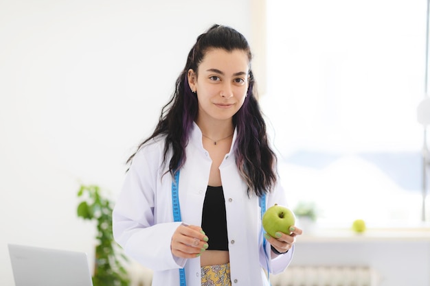 Ernährungsberaterin mit grünem Apfel in der Hand, die im Büro der Gewichtsverlustklinik bleibt