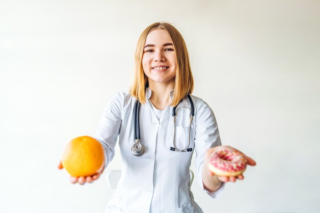 Ernährungswissenschaftlerin, die Orange und Donut in den Händen auf weißem Hintergrund hält