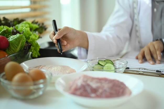Ernährungswissenschaftlerin in weißem Mantel, die am Schreibtisch mit Proteinquellen und Gemüse arbeitet