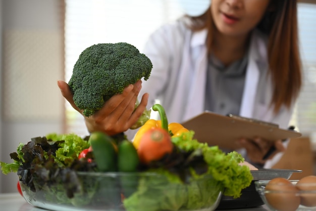 Ernährungswissenschaftlerin in weißem Mantel, die in ihrer Klinik arbeitet und gesundes Gemüse und Obst zeigt