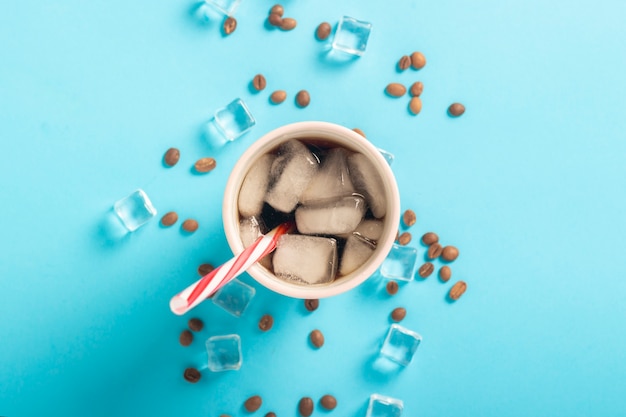 Erneuernder Eiskaffee in einem Glas und in Eiswürfeln und in Kaffeebohnen auf einer blauen Oberfläche. Konzeptsommer, Kolabaum mit Eis, Auffrischungscocktail, Durst. Flachgelegt, Draufsicht