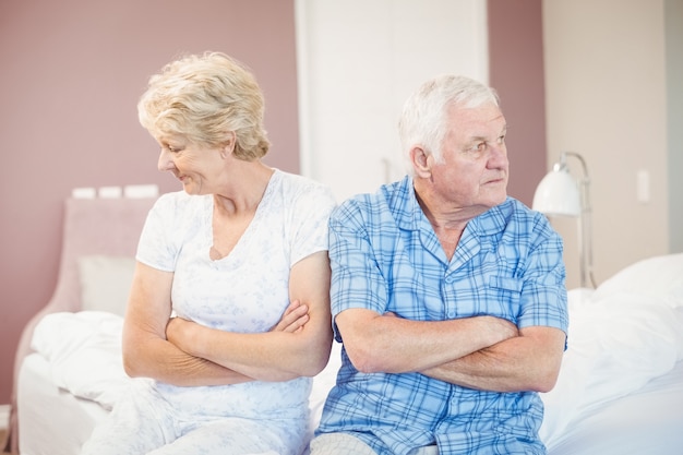 Ernste ältere Paare, die zu Hause auf Bett sitzen