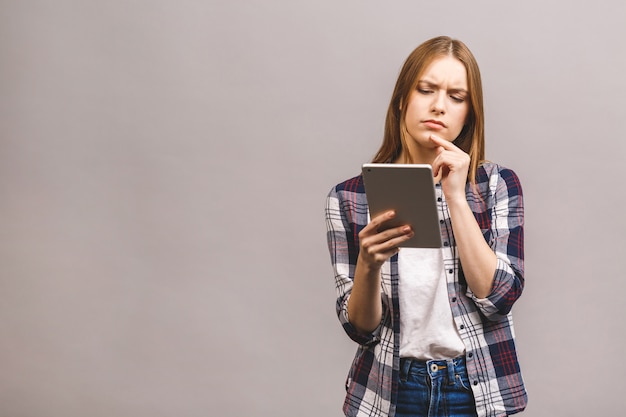 Ernste denkende schöne junge Frau im lässigen unter Verwendung des digitalen Tablets.