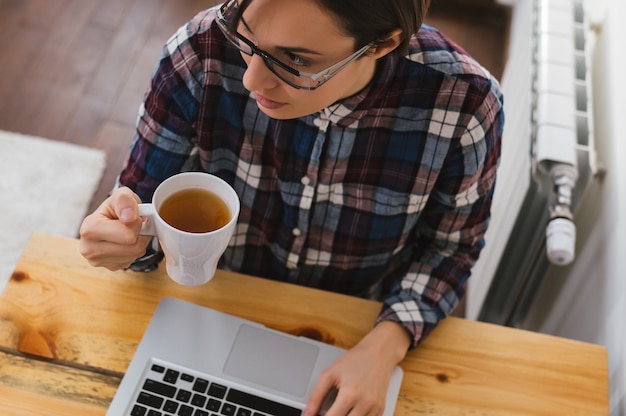 Ernste erwachsene einzelne Frau, die bei Tisch sitzt, Kaffeetasse hält und einen Laptop verwendet