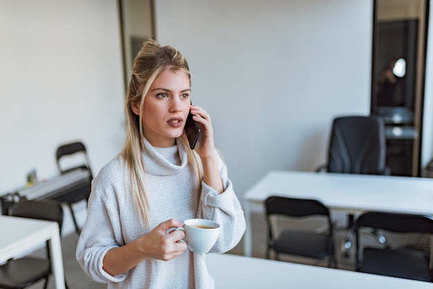 Ernste Geschäftsfrau, die am Telefon auf Kaffeepause spricht.