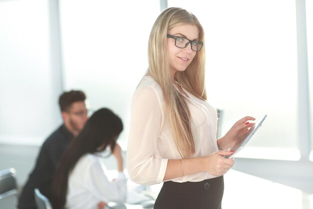 Ernste Geschäftsfrau mit digitalem Tablett, das nahe Schreibtisch steht