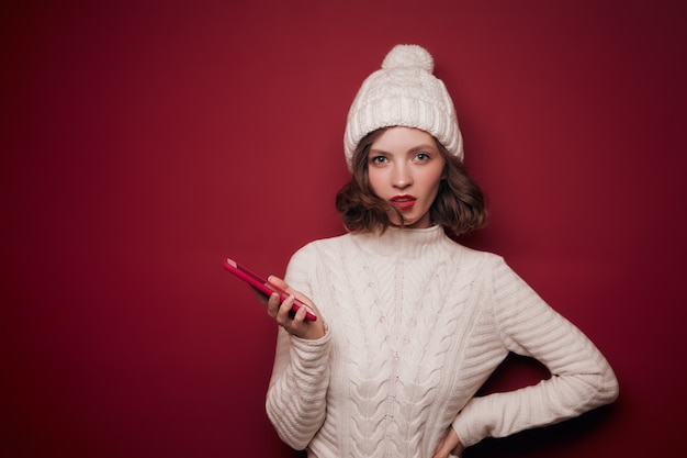 Ernste junge Frau im Pullover hält Telefon