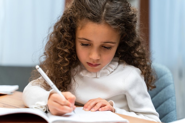 Ernste kleine gemischtrassige lockige Mädchen mit Fernunterricht beim Schreiben von etwas Glückliches kleines Kind lernen online auf dem Computer Stockfoto Homeschooling-Konzept