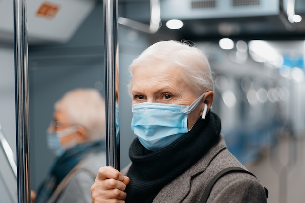 Ernste reife Frau in einer Schutzmaske, die in einer U-Bahn steht