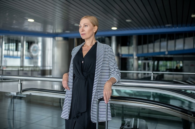 Ernste stilvolle Frau mit Koffer im Flughafenterminal