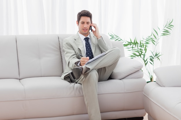 Ernster Geschäftsmann, der auf dem Sofa nennt mit seinem Handy sitzt