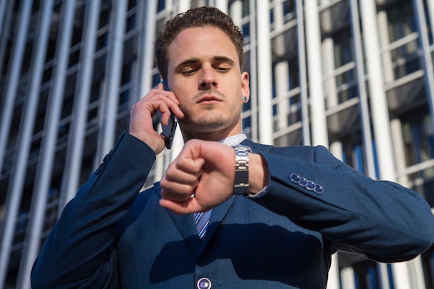 Ernster Geschäftsmann, der die Zeit spricht am Telefon überprüft