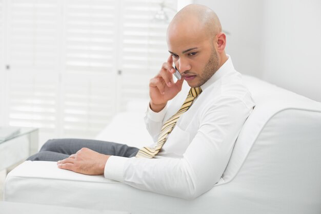 Ernster Geschäftsmann, der zu Hause Mobiltelefon auf Sofa verwendet