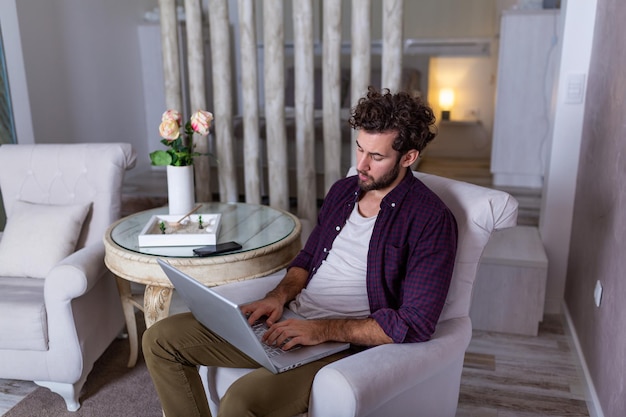 Ernster Geschäftsmann mit ernstem Gesicht, das zu Hause sitzt und Laptop für sein Projekt verwendet. freiberufliche Arbeit von zu Hause aus Geschäftsmann zu Hause, der Statistiken auf Handy und Laptop überprüft