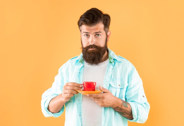 Ernster kaukasischer Mann hält Tasse und Untertasse gelben Hintergrundtee