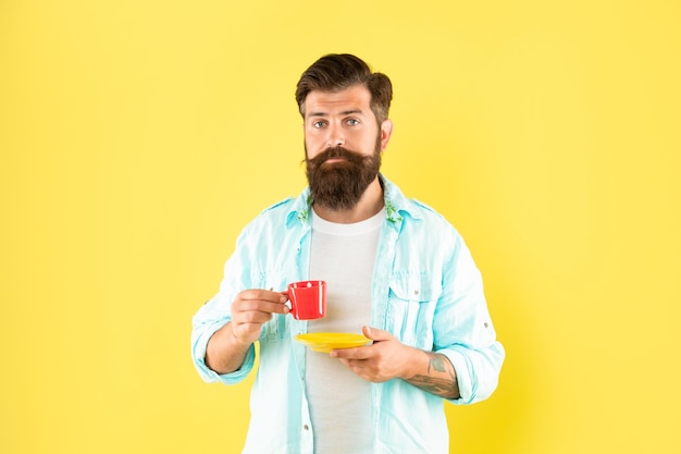 Ernster Kerl, der Kaffee aus der Tasse trinkt, die eine Untertasse mit gelbem Hintergrund hält