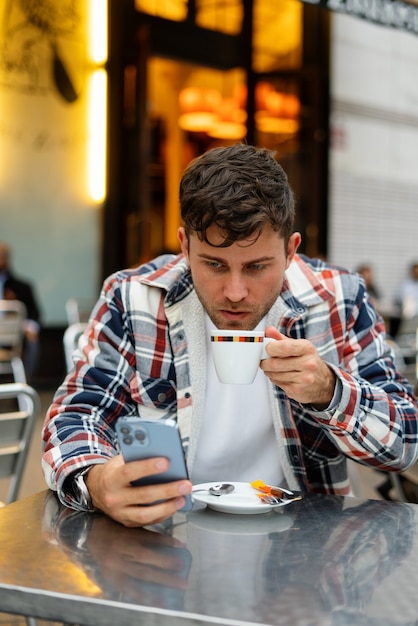 Ernster Mann, der Kaffee trinkt und Smartphone benutzt