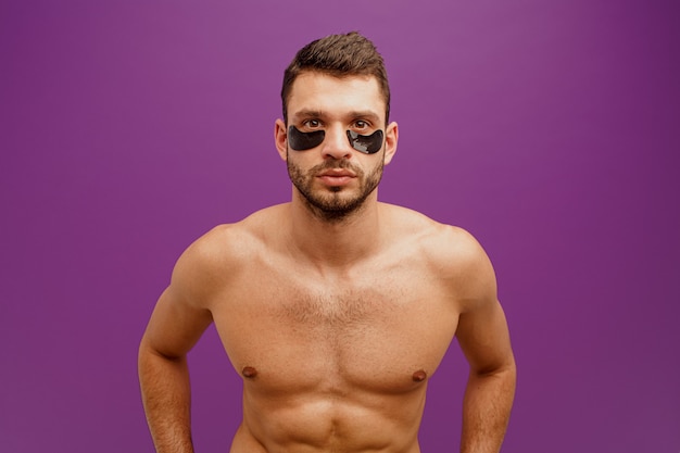 Ernster Mann mit Augenklappe im Gesicht. Bärtiger Kerl mit perfekter Haut, der in die Kamera schaut. Konzept der Gesichtspflege. Auf lila Hintergrund isoliert. Studio-Shooting. Platz kopieren