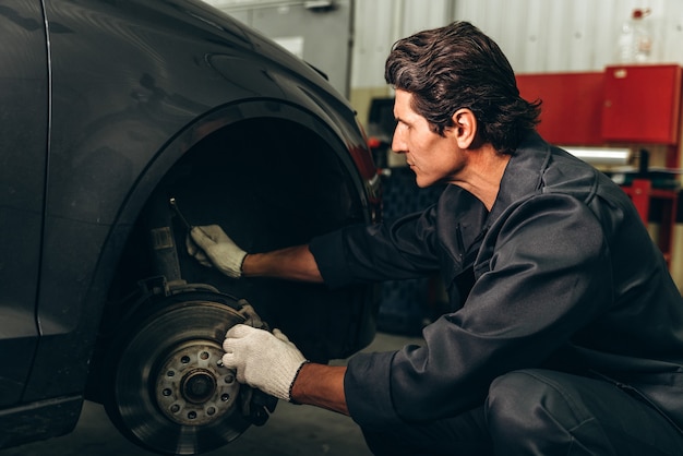 Ernster Mechaniker mit Handschuhen, der sich darauf vorbereitet, ein Rad in ein Auto zu setzen. Auto-Check-up und Auto-Service-Konzept. Stock Foto