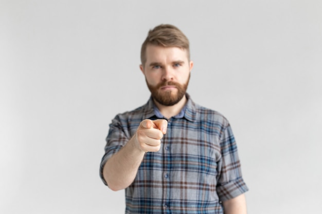 Ernster Studentenmann, der auf der Kamera auf weißem Hintergrund zeigt.